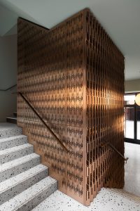 Custom-made laser-cut screen, used as full-height stair balustrading and for feature walls throughout the building, in Double Stone Steel PVD colored stainless steel Bronze Brush