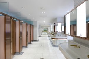 Interior of upgraded toilets at Victoria Rail Station, London showing contrast in cubicle door and surround achieved through turning the grain of the stainless steel 45 degrees. Double Stone Steel PVD colored stainless steel in Rose Gold Hairline. - Faucets, basin band trim and mirror frame in Double Stone Steel PVD colored stainless steel Bronze No Brush. - Client: Network Rail - Architects: Landolt + Brown - Fitout: Maxwood Washrooms