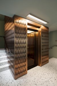 Office upgrade. Custom designed and fabricated laser-cut screen, for stair detailing and as elevator surround, in Double Stone Steel PVD colored stainless steel Bronze Brush