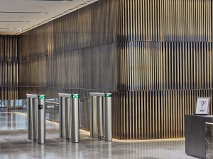 Office development, London. - Interior decorative wall façade of dark wenge timber backing with mounted vertical narrow bars in Double Stone Steel PVD colored stainless steel in Brass Brush.