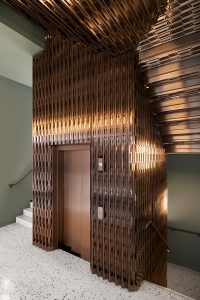 Custom designed and fabricated laser-cut screen, for stair detailing and as elevator surround, in Double Stone Steel PVD colored stainless steel Bronze Brush