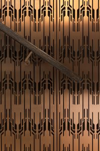 Detail of custom designed and fabricated laser-cut screen used as full-height decorative stair balustrading in Double Stone Steel PVD colored stainless steel Bronze Brush