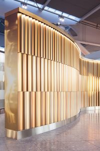 29 meter screen denoting entrance to British Airways Private Check-In and 1st Class Lounge. Fluted sections in Double Stone Steel PVD Colored Stainless Steel Champagne, Chocolate and Almond Gold Brush.