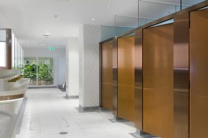 Interior of upgraded toilets at Victoria Rail Station, London showing contrast in cubicle door and surround achieved through turning the grain of the stainless steel 45 degrees. Double Stone Steel PVD colored stainless steel in Rose Gold Hairline. - Faucets, basin band trim and mirror frame in Double Stone Steel PVD coloured stainless steel Bronze No Brush. - Client: Network Rail - Architects: Landolt + Brown - Fitout: Maxwood Washrooms