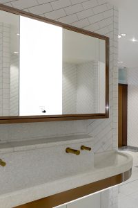 Interior of upgraded toilets at Victoria Rail Station, London. Faucets, basin band trim and mirror frame in Double Stone Steel PVD colored stainless steel Bronze Brush.