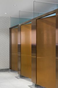 Interior of upgraded toilets at Victoria Rail Station, London showing contrast in cubicle door and surround achieved through turning the grain of the stainless steel 45 degrees. Double Stone Steel PVD colored stainless steel in Rose Gold Hairline.