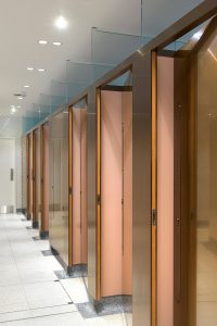 Interior of upgraded toilets at Victoria Rail Station, London showing harmonising color scheme using copper and bronze tones of PVD. Double Stone Steel PVD colored stainless steel in Rose Gold Hairline.