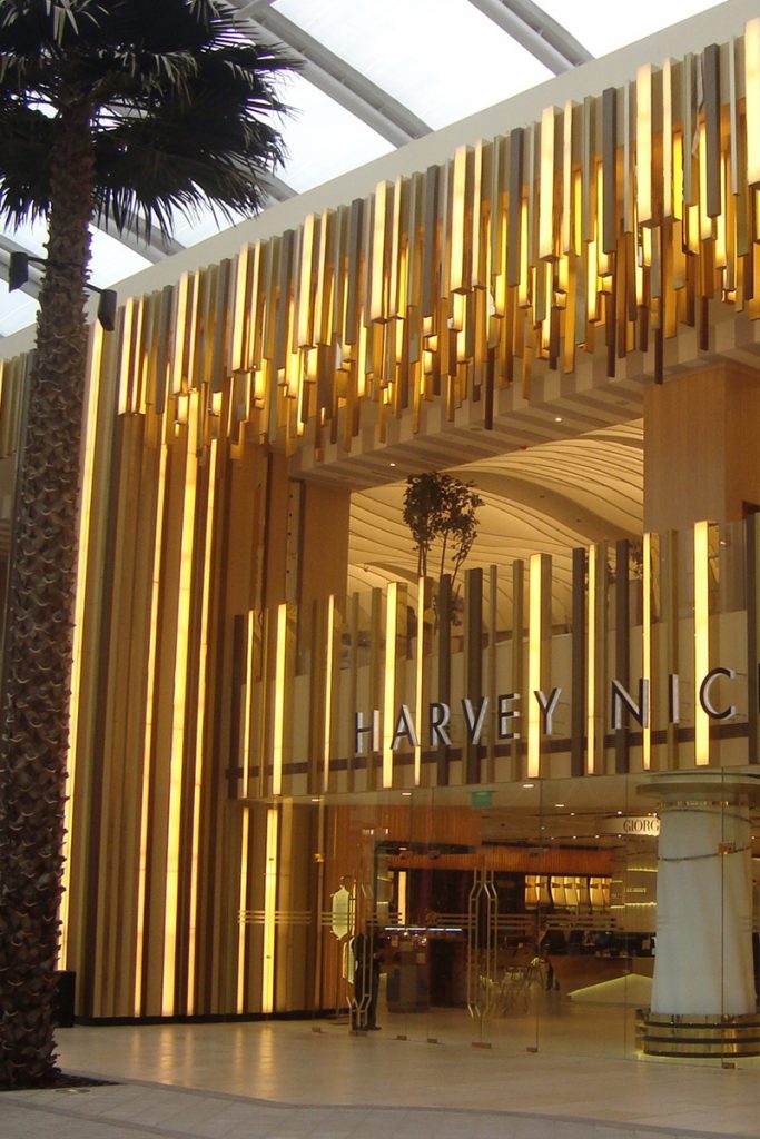 Harvey Nichols retail department store, The Avenues, Kuwait. Undulating façade, columns and detailing in Double Stone Steel PVD colored stainless steel Royal Gold Mirror.
