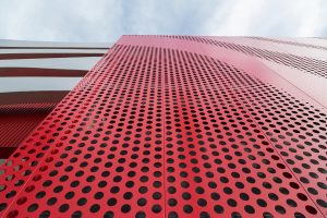 The red-painted perforated aluminium screen that forms a backdrop to the wavy stainless steel Angel Hair ribbons for the façade of The Automotive Petersen Museum, Photography by Tex Jernigan.